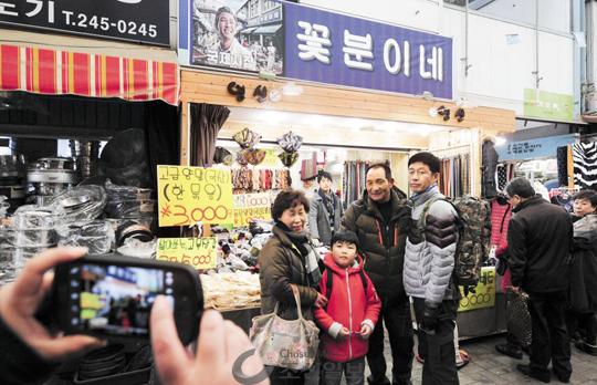 
	영화‘국제시장’이 큰 인기를 끌면서 주인공 덕수가 운영한 가게‘꽃분이네’에 사람들이 몰리고 있다. 원래 이름이‘영신’이었던 이 의류점은 간판을‘꽃분이네’로 바꿔 달았다. 지난 6일 시장을 찾은 사람들이 기념사진을 찍고 있다. 
