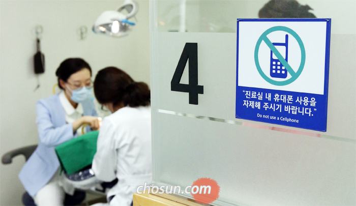 “휴대폰 사용 자제해주세요” - 지난 16일 오후 서울 종로구 서울대 치과병원 진료실 앞에 ‘휴대폰 사용을 자제해 달라’는 경고문이 붙어 있다. 진료 중 휴대폰을 사용하는 환자들이 늘어나자 서울대 치대 병원은 2년 전부터 자제를 당부하는 쪽지를 붙였다.