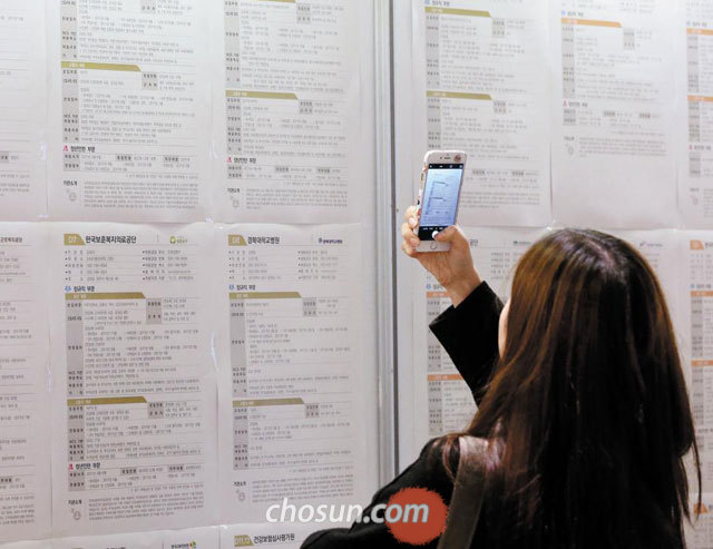 한 취업 준비생이 휴대전화로 벽에 걸린 취업 정보를 찍어 저장하고 있다.