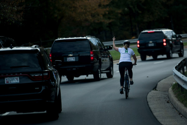 도널드 트럼프 미국 대통령이 탄 차량행렬이 28일(현지시간) 버지니아주 스털링의 트럼프 내셔널 골프클럽을 빠져나가고 있는 가운데 자전거를 타고 가던 한 여성이 차량을 바라보며 왼손을 들어 가운뎃손가락을 치켜세우고 있다./연합뉴스