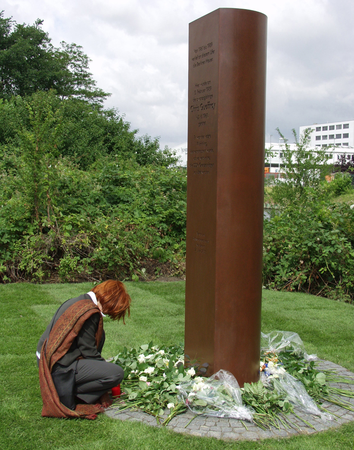 2003년 6월 독일 베를린 브리츠지구의 운하 곁에서 크리스 게프로이를 위한 기념비 제막식이 열렸을 때 크리스의 모친 카린 게프로이가 기념비 옆에 앉아 아들을 추모하고 있다. 1989년 2월 동베를린에 살고 있던 만 20세의 청년 크리스 게프로이는 친구와 함께 베를린 장벽을 넘어 서독으로 탈출하려다가 동독 국경수비대의 총격을 받고 숨졌다. 그는 베를린 장벽을 넘다가 국경수비대의 발포로 숨진 마지막 동독인이었고, 독일 정부는 통일 후에도 관련자들은 찾아내 처벌했다.