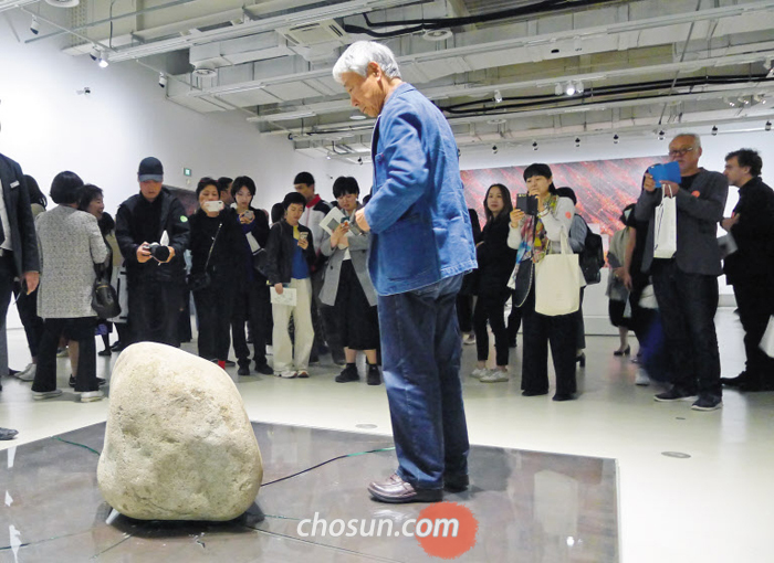 이우환이 중국 상하이 PSA 전시장에 놓인 ‘관계항―모멘텀’ 위에 섰다. 돌을 들었다 놔 유리를 깨뜨린 직후다. 이우환은 그 위에 올라가 발을 구르며 유리를 더 깨부쉈다.
