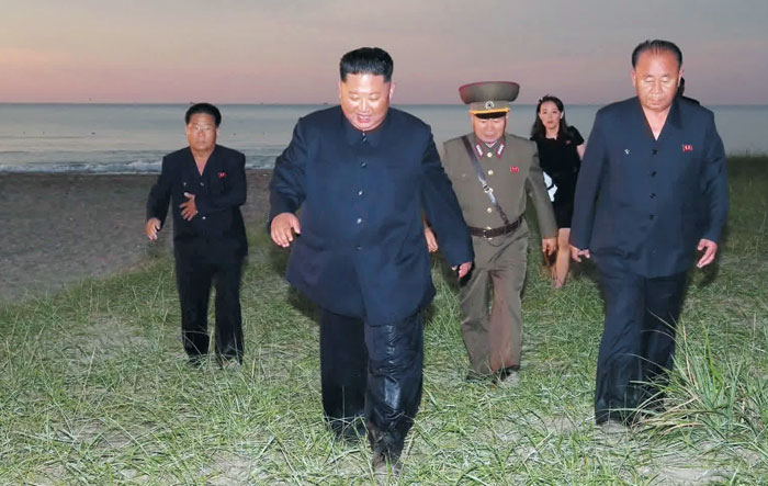 김정은 북한 국무위원장이 지난 24일 '초대형 방사포' 발사를 참관하기 위해 인민복 차림으로 바다에 들어갔다가 나와 참모들과 함께 풀밭을 가로질러 가고 있다.