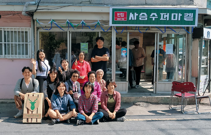 전라남도 목포 구도심에서는 지난해 8월부터 '괜찮아마을' 프로젝트가 진행 중이다. 전국에서 모인 청년들은 이곳 주민으로 지내며 지역 자원을 활용해 다양한 실험을 한다. 사진은 팝업 갤러리로 변신한 구도심의 수퍼마켓 앞에서 괜찮아마을 청년들과 지역 어르신들이 기념 촬영을 하는 모습.