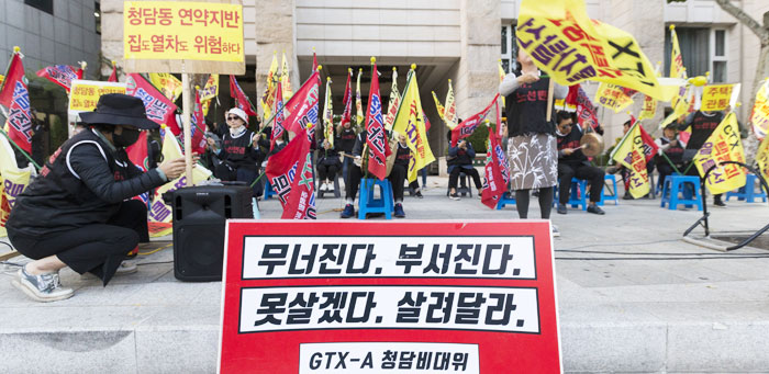 지난 22일 서울 강남구 청담동 도로변에서 청담동 주택가 지하로 수도권광역급행철도(GTX)-A 노선이 통과하는 걸 반대하는 주민들이 '주택붕괴' '열차탈선' 등이 쓰인 깃발을 들고 시위를 벌이고 있다.