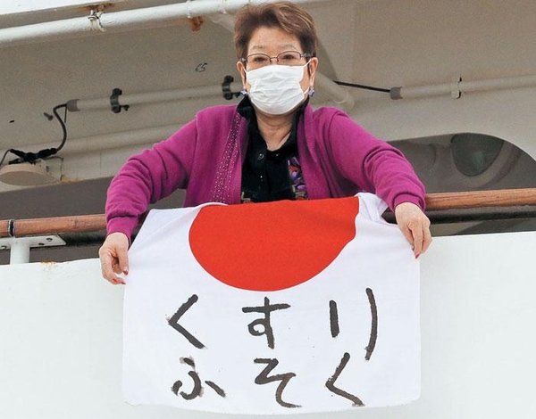 일본 근해에 정박한 다이아몬드 프린세스호에 탄 한 승객이 7일 마스크를 낀 채 '쿠스리 후소쿠(약 부족)'라고 적힌 일장기를 내걸며 도움을 호소하고 있다. /로이터 연합뉴스