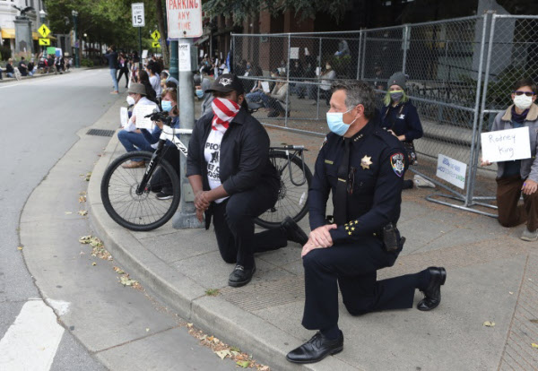 지난달 30일(현지 시각) 미 캘리포니아 샌타크루즈시 도심에서 앤디 밀스(오른쪽) 경찰서장과 저스틴 커밍스(가운데 시장이 연대의 뜻으로 시위대 수백명과 함께 무릎을 꿇고 있다./AP 연합뉴스
