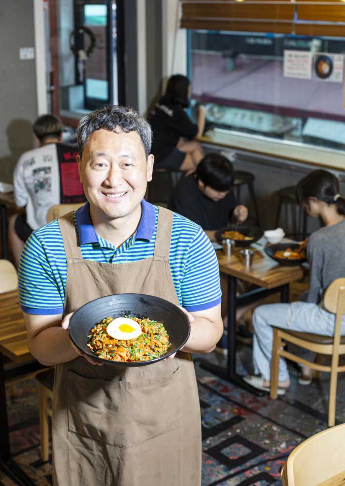 지난 21일‘청년밥상 문간’에서 주인 이문수 신부가 ‘김치 고기 덮밥’을 들어 보이고 있다. 큰 대접에 쌀밥을 가득 담고 잘 익은 김치와 돼지고기를 얹었다. 한 그릇 3000원 / 김종연 영상미디어 기자
